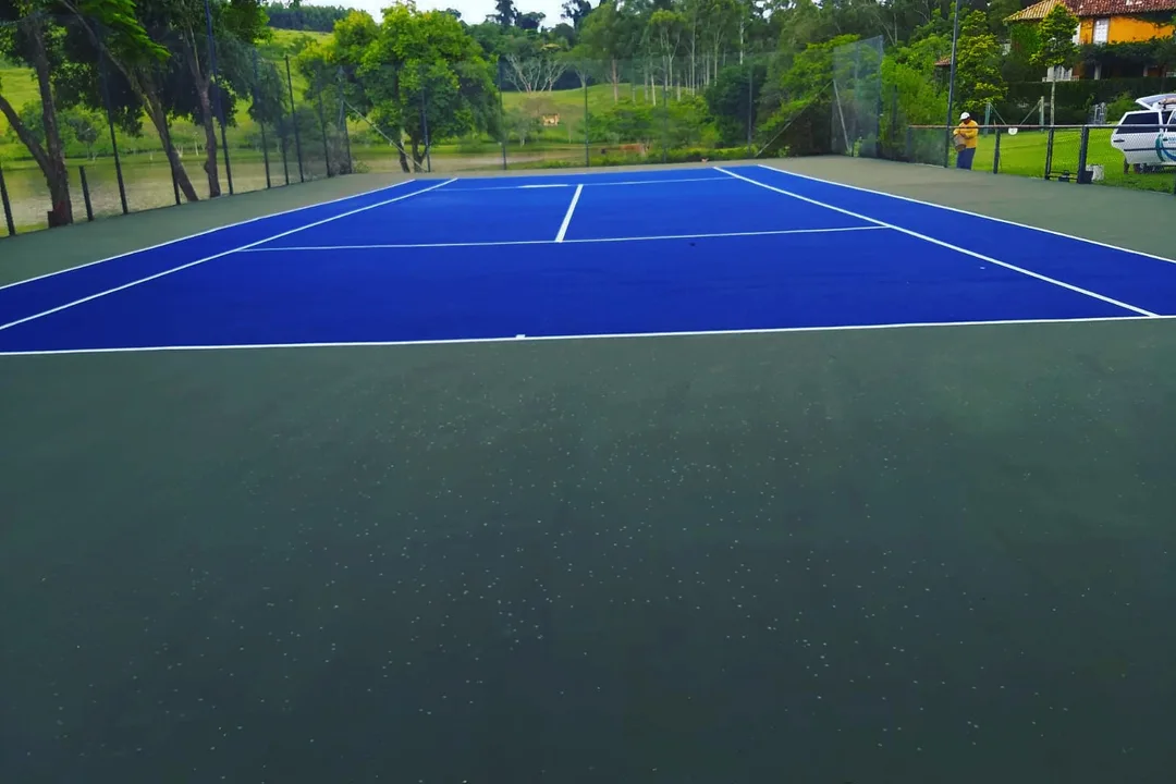 Foto do acervo da Pratika Sport: quadra de tênis azul em espaço arborizado